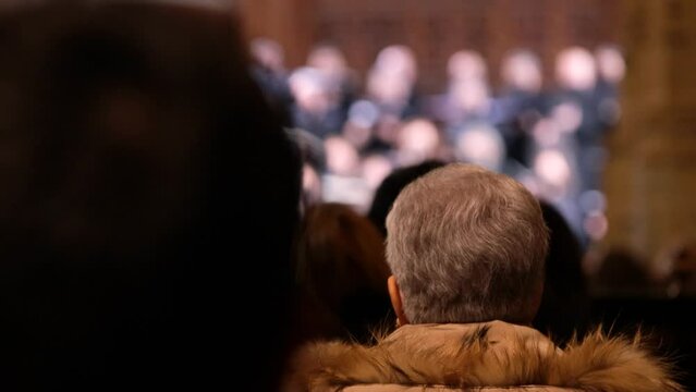 Old woman with gray hair rear shot, admiting a chorus concert indoors. Back view of a senior woman head in 4k.