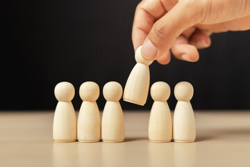 Wooden figures human was chosen leadership of teamwork. man's hands are select wooden puppet to...