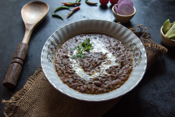Daal makhni or dal makhani is a north Indian recipe using black lentils and red kidney beans served in a bowl on a dark background. Close up, selective focus.