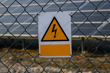 Solar panel farm live, fence. High voltage sign with solar panels in background.
