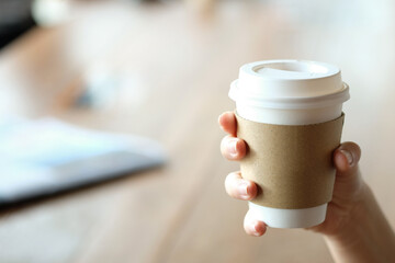 Hand holding paper cup of hot coffee in cafe