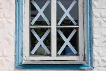 The window of a rural house is sealed with strips of paper. Protection of glass from a blast wave. War in Ukraine.