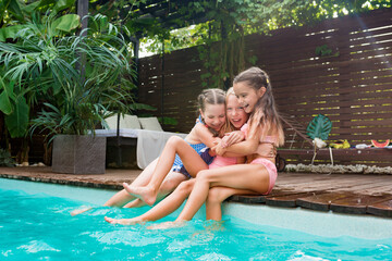 Summertime lifestyle. Girls having fun and relaxing by swimming pool. Kids sitting at poolside and...