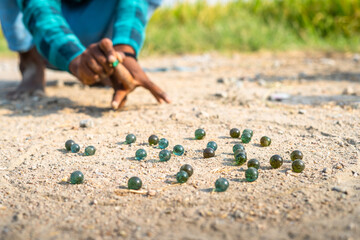 close up shot of kid plyaing by hitting goli or glass marbles on roadside at Indian village -...