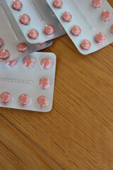 Pharmaceutical medicine capsules on wooden table. Pink round pills in blister packaging