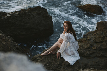 woman with wet hair barefoot in a white dress sits on a cliff nature unaltered