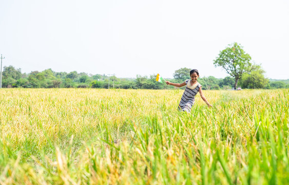 Dancing young village girl kid by holding indian flag at pady agriculture field - concept of freedom, republic or independence celebration and rural India.