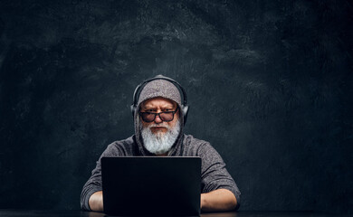 Shot of contemporary senior man with headphones and laptop sitting at table.