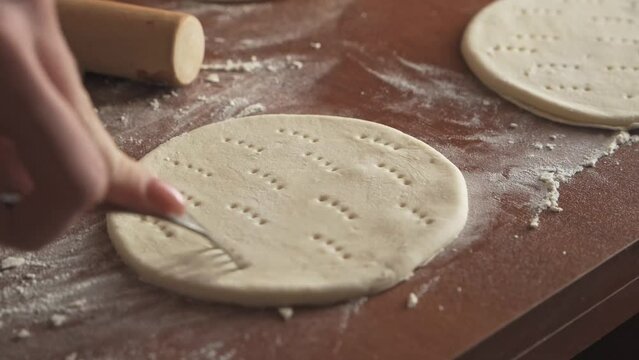 Women's hands, using a rolling pin, roll out the dough for baking.