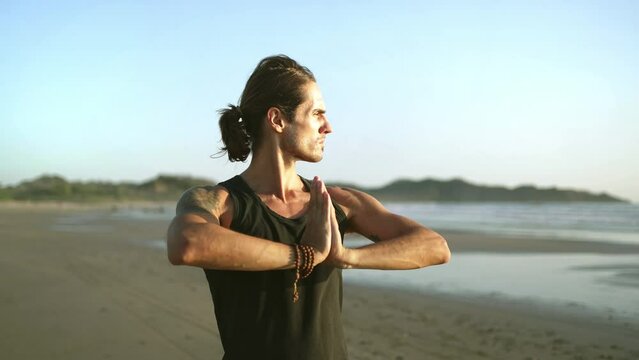 Young millennial yogi man practicing Qi gong,  tai chi yoga on beach. Healthy active, mindfulness wellness lifestyle. wellbeing, peaceful relaxation. traditional chinese martial arts.