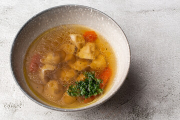 Tasty chicken soup bouillon with dumplings, chicken meat and parsley in a white bowl. Isolated on marble background. Healthy meal menu.
