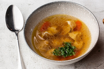 Tasty chicken soup bouillon with dumplings, chicken meat and parsley in a white bowl. Isolated on marble background. Healthy meal menu.