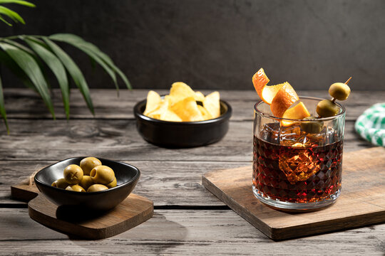 Vermouth cocktail with snacks on wooden base on dark background. Typical spanish appetizer..
