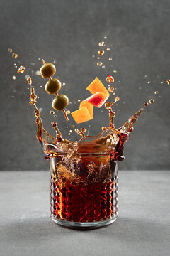 Vermouth cocktail splashing out of glass on light gray background. Vertical format.