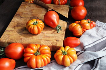 Fresh ripe hairloom tomatoes and knife on rustic wooden board over dark background
