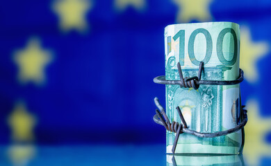 European Union currency wrapped in barbed wire against flag of EU as symbol of Economic warfare, sanctions and embargo busting. Horisontal image. Copy space.