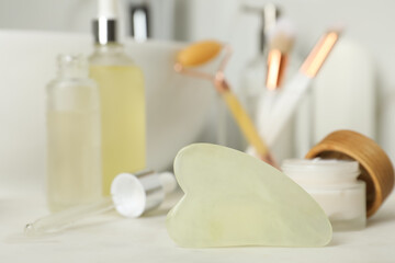 Fototapeta na wymiar Jade gua sha tool and toiletries on white countertop in bathroom, closeup