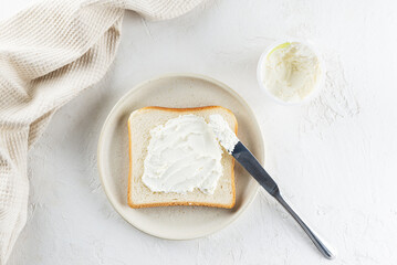 Toast bread spread with cream cheese in a plate on a light table, top view.