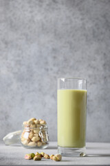 Pistachio milk in glass and pistachios in glass jar on gray background. Lactose free. Vegan nutty plant based milk. Vertical.