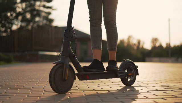 Girl rides an electric scooter. Child travel cheerfully. Empty city street. Legs on an electric scooter. Girl travel on scooter. Child on deserted street. Electric scooter close up. City travel girl