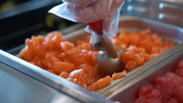 Gloved hand scoops salmon, worker turns chopped salmon on poke bowl bar, close up slow motion 4K