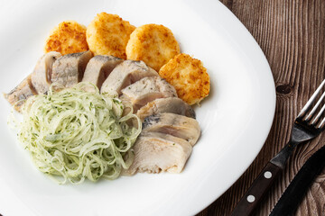 Herring with potatoes and onions on a plate. Ukrainian traditional cuisine on wooden background.