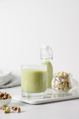 Pistachio milk in glass and pistachios in glass jar on white background. Lactose free. Vegan nutty plant based milk. Vertical.