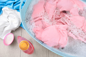 Basin with pink garment near bottle of detergent and powder on floor, flat lay. Hand washing laundry