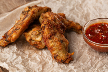 Fried Chicken Wings Covered in True Hot BBQ Sauce served with red hot chilli sauce on a parchment paper on wooden background.