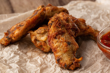 Fried Chicken Wings Covered in True Hot BBQ Sauce served with red hot chilli sauce on a parchment paper on wooden background.