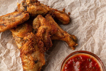 Fried Chicken Wings Covered in True Hot BBQ Sauce served with red hot chilli sauce on a parchment paper on wooden background.