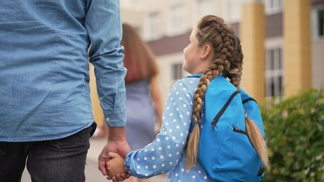 Happy family. Father and daughter go to school. Schoolgirl with backpack holds her father hand. Family goes to school. Male hand helping child. Father and daughter schoolgirl are walk in school park