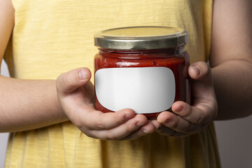 Closeup shot of a little girl holding a homemade tomato paste jar with an empty white label on it