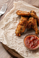 Fried Chicken Wings Covered in True Hot BBQ Sauce served with red hot chilli sauce on a parchment paper on wooden background.