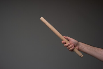 Wooden kitchen rolling pin held in hand by Caucasian male. Close up studio shot, isolated on gray background