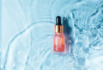 Mockup of cosmetic glass pink bottle with pipette and serum on water surface