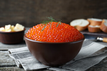 Bowl with delicious red caviar and dill on wooden table