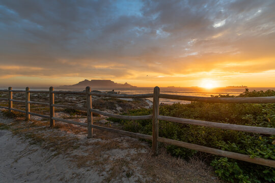 View of the golden sun setting in a deep blue cloudy sky from behind a wooden face in Blouberg near