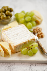 Cheese platter with organic cheeses - blue cheese cheddar, emmantaler, french soft cheese with strong smell, italian parmesan, grapes, tomatoes, olives, nuts and crackers on marble board