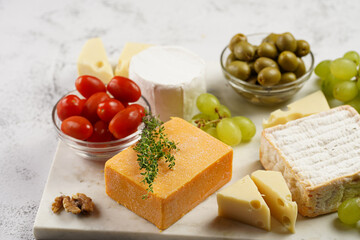 Cheese platter with organic cheeses - blue cheese cheddar, emmantaler, french soft cheese with strong smell, italian parmesan, grapes, tomatoes, olives, nuts and crackers on marble board