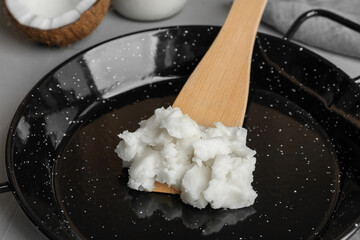 Frying pan with coconut oil and wooden spatula on light grey table, closeup