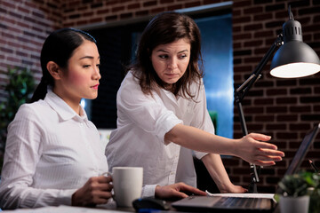 Multiethnic colleagues discussing about startup project documentation while looking at charts on laptop. Marketing company employee getting help from manager regarding wrongly issued accounting data