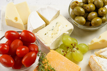 Cheese platter with organic cheeses - blue cheese cheddar, emmantaler, french soft cheese with strong smell, italian parmesan, grapes, tomatoes, olives, nuts and crackers on marble board
