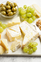 Cheese platter with organic cheeses - blue cheese cheddar, emmantaler, french soft cheese with strong smell, italian parmesan, grapes, tomatoes, olives, nuts and crackers on marble board