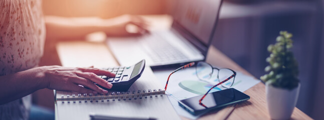 Woman working with laptop and calculator at home office - 501496141