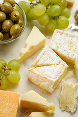 Cheese platter with organic cheeses - blue cheese cheddar, emmantaler, french soft cheese with strong smell, italian parmesan, grapes, tomatoes, olives, nuts and crackers on marble board