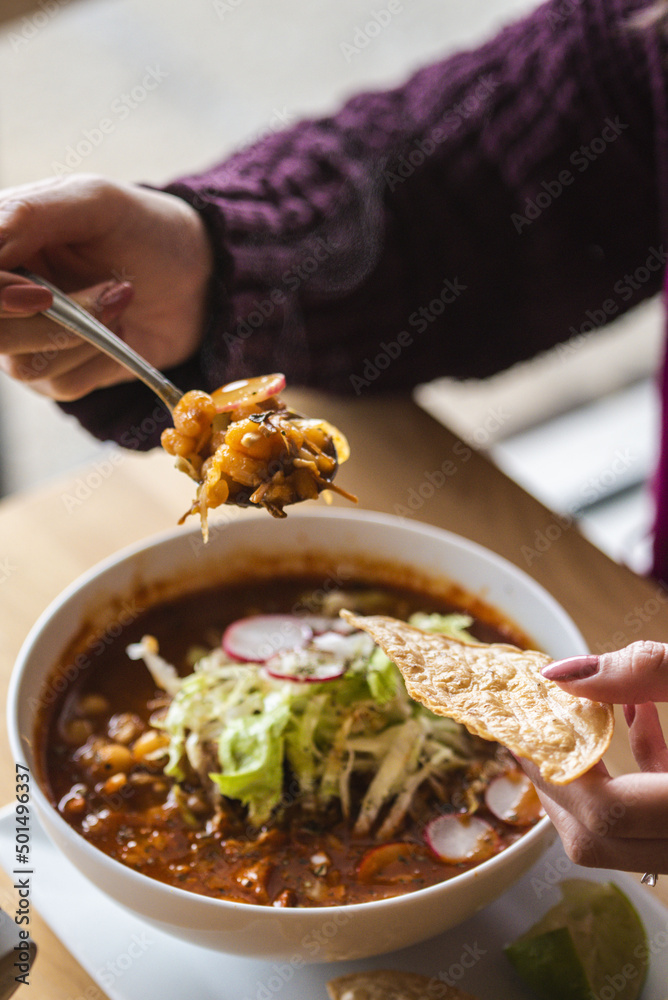 Poster vertical closeup shot of a person eating a freshly served mexican pozole with lime