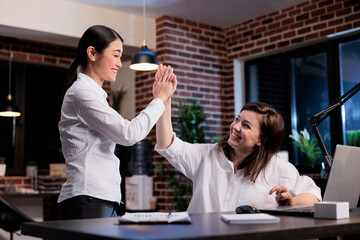 Happy motivated businesswomen in office workspace celebrating successful business deal by highfiving each other. Positive excited multiethnic work colleagues expressing achievement.