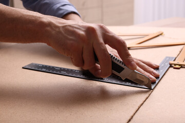 Man cutting chip board with utility knife and ruler indoors, closeup - obrazy, fototapety, plakaty