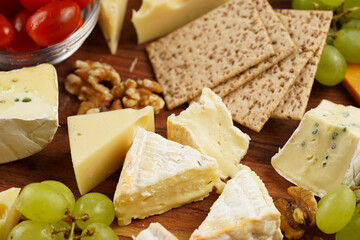 Cheese platter with organic cheeses - blue cheese cheddar, emmantaler, french soft cheese with strong smell, italian parmesan, grapes, tomatoes, olives, nuts and crackers on wooden board